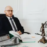 Prawnik w okularach siedzi przy biurku, obok statuetki Temidy. Zastanawia się, ile wynosi taksa notarialna.