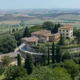 Un borgo toscano con casali in pietra e un edificio giallo, immerso nel verde e con dolci colline sullo sfondo. Castelnuovo Tancredi, un'oasi di pace.