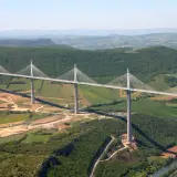 Najwyższy most w Europie, Viadukt Millau, przecina zieloną dolinę z imponującymi pylonami i stalowymi linami.