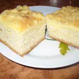 Puszyste ciasto drożdżowe z serem, posypane kruszonką, prezentuje się apetycznie na białym talerzu.