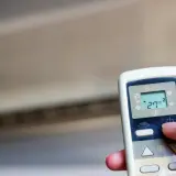 Mano ajustando el control remoto de un aire acondicionado cool o heat. La pantalla muestra 27°C.