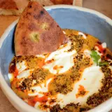 Un bol de cilbir recette, avec du pain pita trempé dans une sauce crémeuse et épicée, garni d'herbes fraîches.