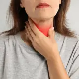 Kobieta dotyka szyi z zaczerwienieniem, co może symbolizować problemy z tarczycą, takie jak niedoczynność tarczycy a menopauza.
