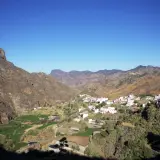 Pueblo blanco de Tejeda, Gran Canaria, con montañas escarpadas y campos verdes en un día soleado.