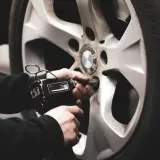 Mano usando una llave de impacto para cambiar ruedas delanteras por traseras en un coche BMW.