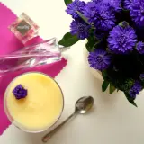 Perfumy "Hypnose" obok deseru i fioletowych kwiatów.