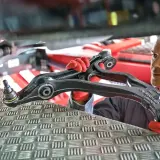 Mechanik w czerwonych rękawiczkach prezentuje element zawieszenia samochodu.