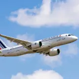 Airbus A220-300 linii Air France wzbija się w błękitne niebo z białymi chmurami.