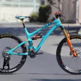 A turquoise Yeti SB6c mountain bike with orange accents, featuring Maxxis tires and Fox suspension, ready for any trail.