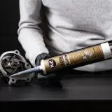 Rękawiczki i pistolet z czarnym silikonem K2. Aplikacja uszczelniacza na element pompy wodnej. Dowiedz się, jak długo schnie silikon.