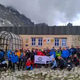 Grupa turystów pozuje do zdjęcia przed drewnianym schroniskiem górskim z flagą.