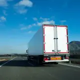 Biała naczepa ciężarówki na autostradzie, przewożąca fracht. Co to jest fracht? To towar w transporcie.