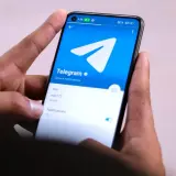 Dłonie trzymają smartfon z otwartą aplikacją Telegram. Widać logo i opcje powiadomień, idealne do dyskretnych rozmów w tajnych grupach Telegram.