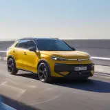 Żółty Volkswagen Cross pędzi po drodze, błyszcząc w słońcu.