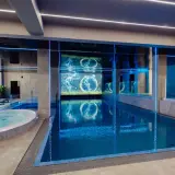 Nowoczesny basen i jacuzzi w rezydencji Aqua Szklarska Poręba. Niebieskie podświetlenie i ekran z animacją tworzą relaksującą atmosferę.