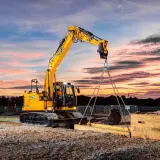 Operator koparki kurs: żółta maszyna JCB podnosi ciężki element na tle zachodzącego słońca.