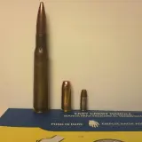 Trois cartouches de tailles différentes, dont une imposante de calibre 50 en mm, posées sur une boîte bleue et jaune.