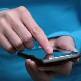 Palec dotyka ekranu smartfona, szukając rozwiązania, jak wyłączyć tryb awaryjny w telefonie.