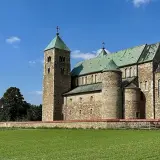 Romańska bazylika tum pod Łęczycą, z zielonymi dachami i kamiennym murem, na tle błękitnego nieba.