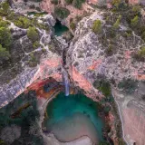 Cascada cayendo en una poza turquesa, rodeada de rocas rojizas y vegetación. Un rincón secreto, como la cueva turche, esperando ser descubierto.