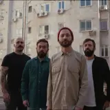 Czterech mężczyzn na tle bloku mieszkalnego, jakby z planety Zeusa.