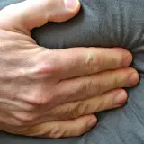Eine Hand drückt auf den Bauch, was auf Beschwerden wie bei einer Lebensmittelunverträglichkeit hindeuten könnte.