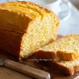 Plumcake senza yogurt dorato e soffice, tagliato a fette su un tagliere di legno con un coltello.
