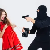 Una mujer con vestido rojo grita mientras un ladrón enmascarado le apunta con una pistola y tira de su bolso. Es como soñar que te roban.