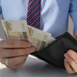 Mężczyzna w koszuli i krawacie wkłada banknoty 200 zł do portfela. Może to być wypłata, premia lub odprawa pośmiertna.