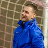 Uśmiechnięty piłkarz w niebieskiej kurtce, gotowy do gry w stylu tiki-taka.