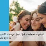 Trzy uśmiechnięte przyjaciółki przytulają się. To obraz codziennego pisania z koleżanką, które wzbogaca życie.