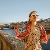 Kobieta w okularach i wzorzystym szalu na tle florenckiego mostu. Popielniczka po włosku, czyli piękny widok.