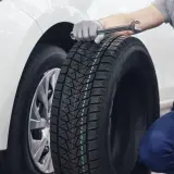 Mecánico con llave inglesa y neumático nuevo, evitando una multa por ruedas caducadas. Pulgar arriba.