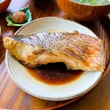 A perfectly cooked piece of karei no nitsuke, its skin crisped and glazed, rests in a savory sauce. Served with pickled plum and okra.