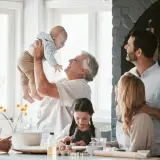 Radosna rodzina w kuchni. Dziadek podrzuca wnuka, babcia patrzy z uśmiechem. Dzieci pieką ciasteczka. To są prawdziwe babciowe dla kogo!