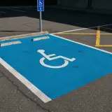 Niebieskie miejsce parkingowe dla niepełnosprawnych, oznaczone symbolem wózka, jest częścią wspólnoty dbającej o dostępność.