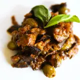 Un saporito piatto di caponata di pesce spada, con melanzane, olive e basilico fresco, pronto per essere gustato.
