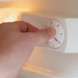 Dłoń kręci pokrętłem termostatu w lodówce, ustawiając temperaturę.