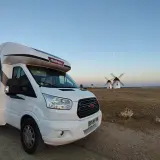 Un camping-car blanc est garé devant des moulins à vent au coucher du soleil. Un voyage en camping-car inoubliable.