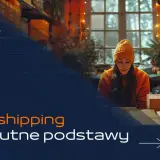 Kobieta w pomarańczowej czapce uczy się, jak zacząć dropshipping, siedząc przy biurku w magazynie pełnym paczek.