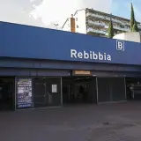 Ingresso della metro Rebibbia a Roma, con insegna blu e lettere bianche. Edifici residenziali sullo sfondo.