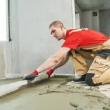 Budowlaniec wyrównuje świeży jastrych za pomocą łaty.
