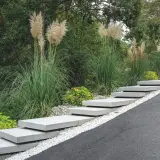 Moderne Treppe aus trockenbeton-Platten, umgeben von Ziergräsern und Kies.