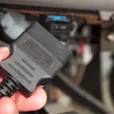 Dłoń trzyma czarny adapter OBD II, gotowy do podłączenia do złącza diagnostycznego pojazdu.