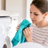 Kobieta wącha świeżo wyprane ubranie, zastanawiając się, dlaczego pranie śmierdzi po wysuszeniu.
