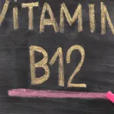 Kreidezeichnung "VITAMIN B12" auf einer Tafel, daneben eine Hand mit pinker Kreide.