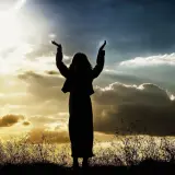 Sylwetka osoby z rękami w górze, na tle dramatycznego nieba, jak w psalm 47.