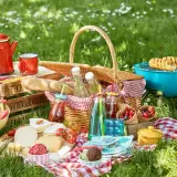 Idealne jedzenie na piknik: kosz pełen smakołyków, grillowana kukurydza, sery, owoce i napoje.