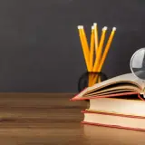 Stos książek, lupa i ołówki na biurku. Idealne do nauki lektury klasa 5.
