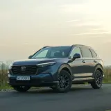 Ciemnoniebieski Honda CR-V Hybrid na tle zachodzącego słońca, zaparkowany na poboczu drogi.